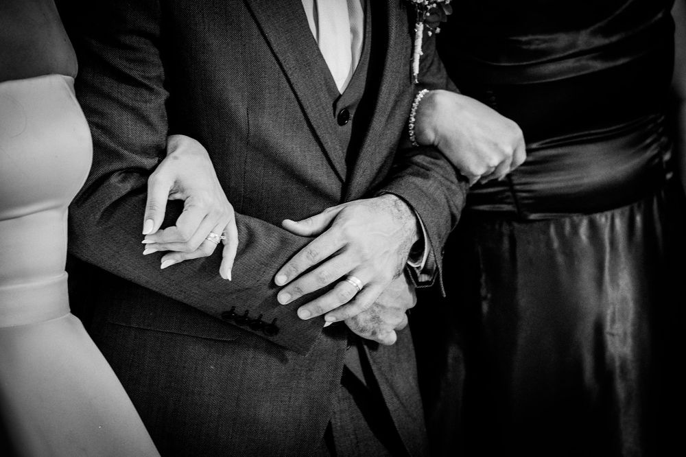 Black and white photo of a couple holding hands, showcasing wedding rings, in formal attire at a wedding ceremony.