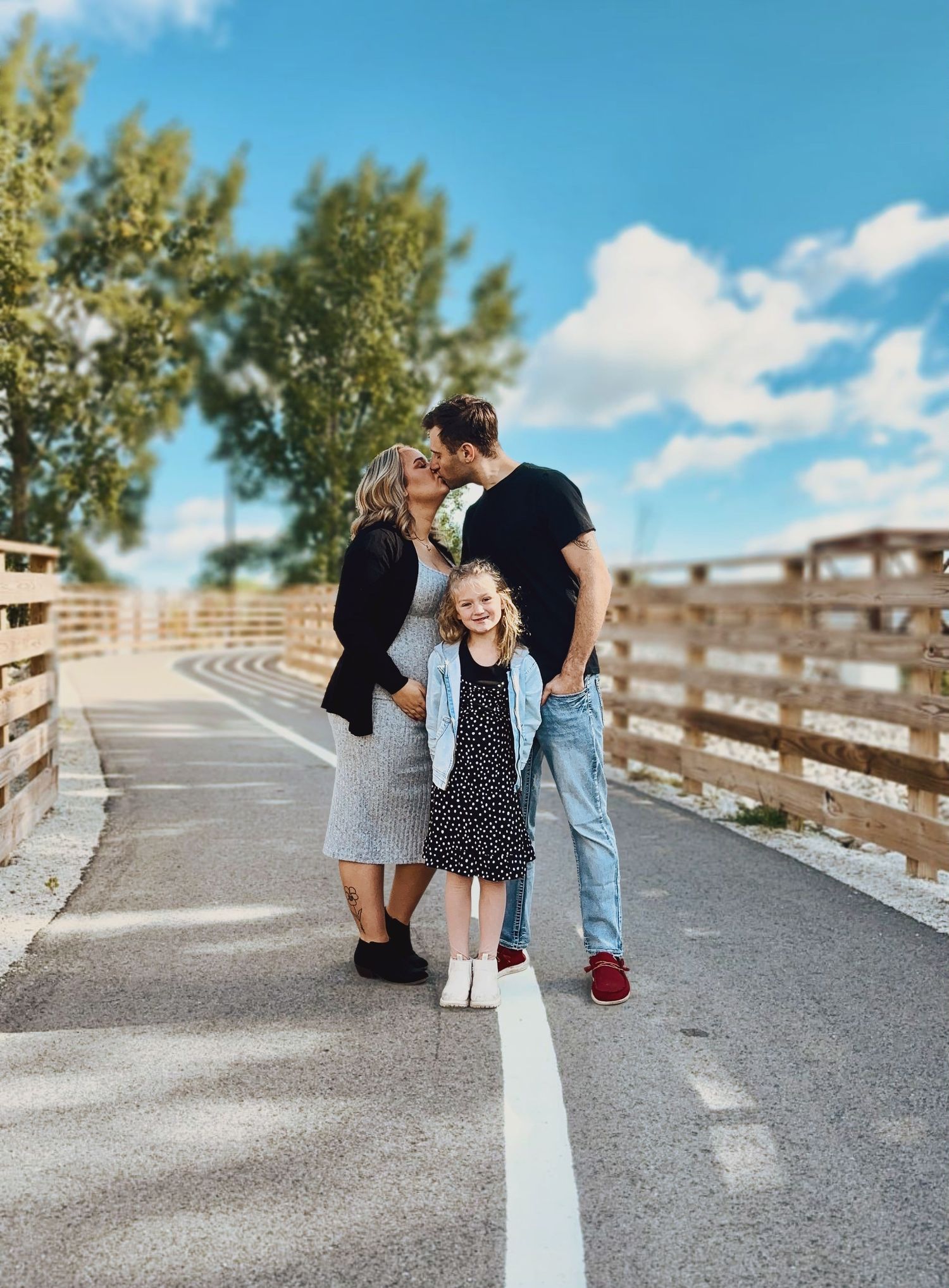 Family photography session with mom and dad kissing and child smiling at camera