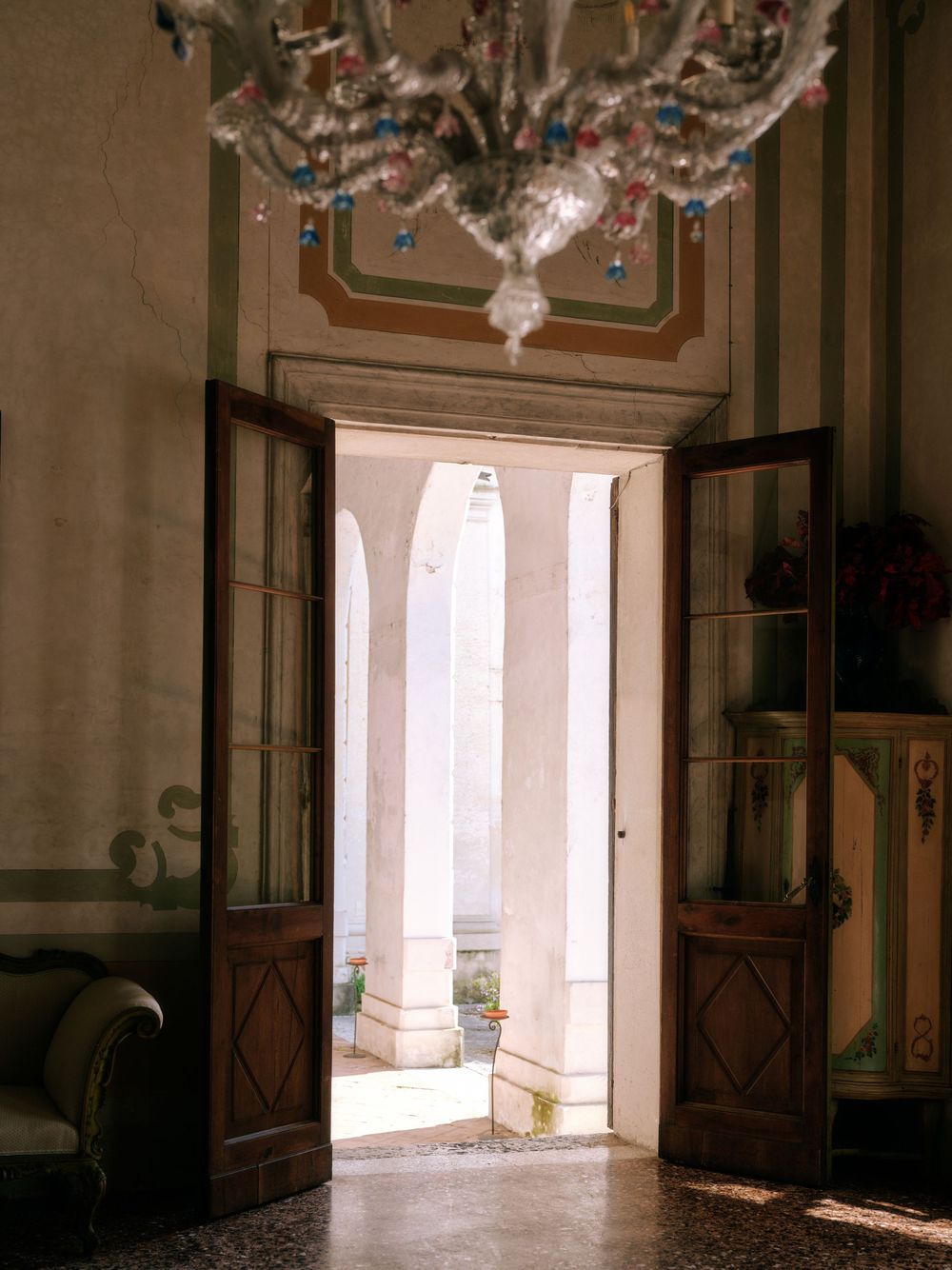 A dimly lit interior hallway with ornate architectural details and a bright window at the end creates dramatic lighting.