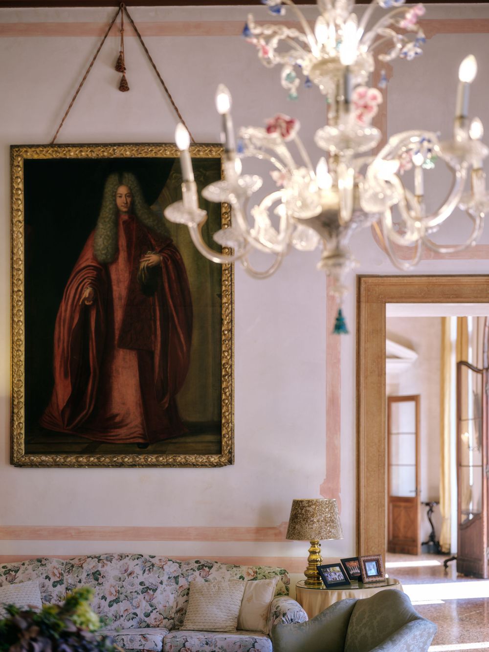 An elegant living room features ornate chandeliers, antique portraits, and floral-patterned furniture in a classic setting.
