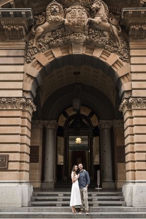 Couple embracing under ornate stone archway with lion crest at historic neoclassical building entrance.