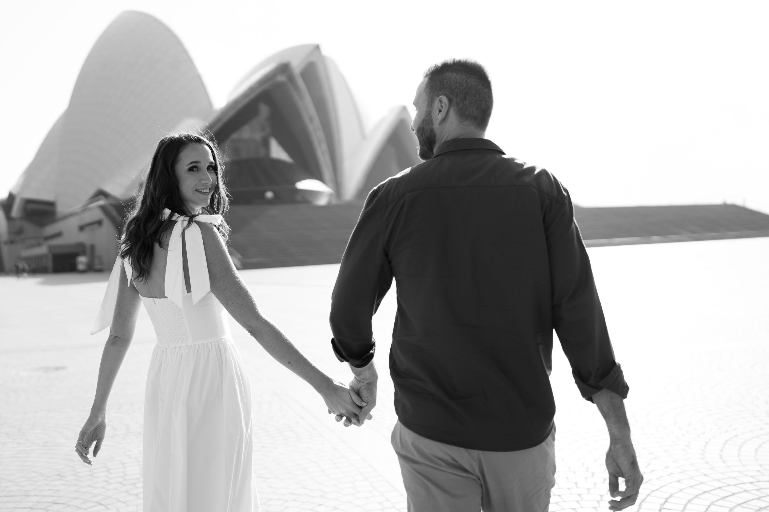 Black and white photo of a couple holding hands near the Sydney Opera House during an engagement shoot.