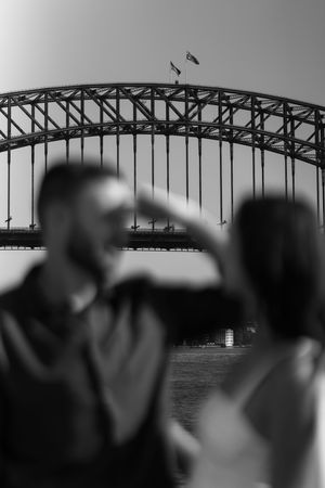 Black and white photo of a couple in soft focus with Sydney Harbour Bridge in the background.