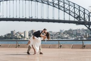 Couple dancing romantically in front of Sydney Harbour Bridge on a sunny day.