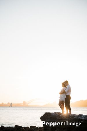 Couple embracing on rocks at sunset with Sydney Harbour Bridge in the background.