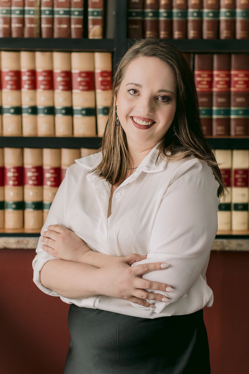 Professional woman in white blouse smiling with arms crossed in front of law library bookshelves.
