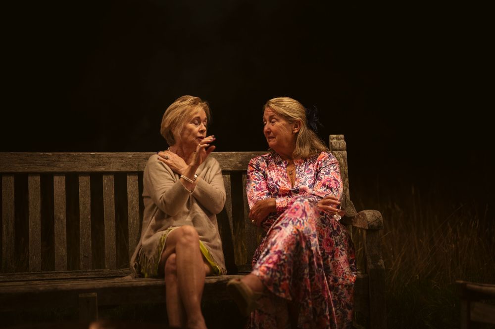 Two female wedding guests sitting together on a bench at night at a Surrey wedding