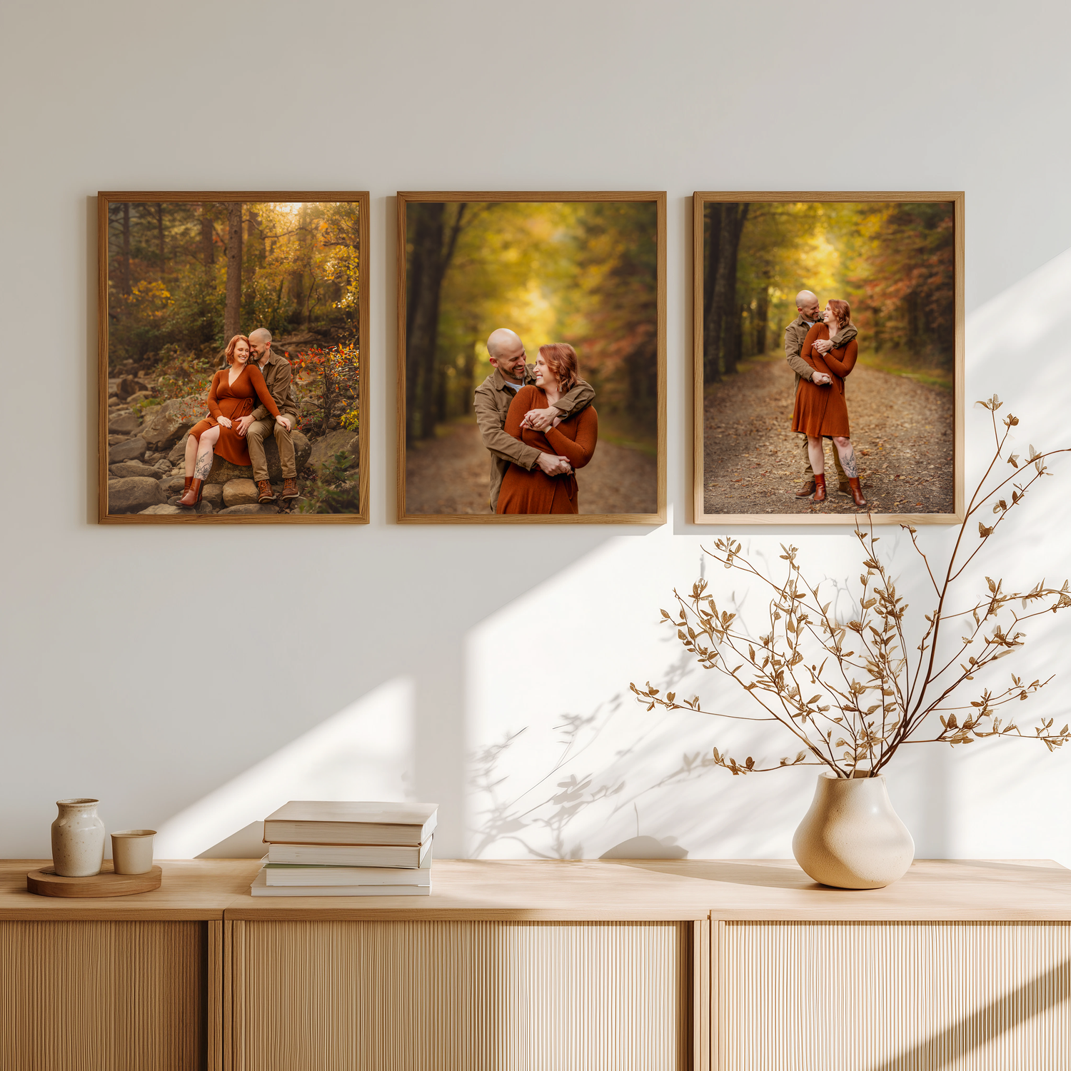 Three autumn forest family photos in wooden frames displayed on a white wall above a wooden sideboard with a vase.
