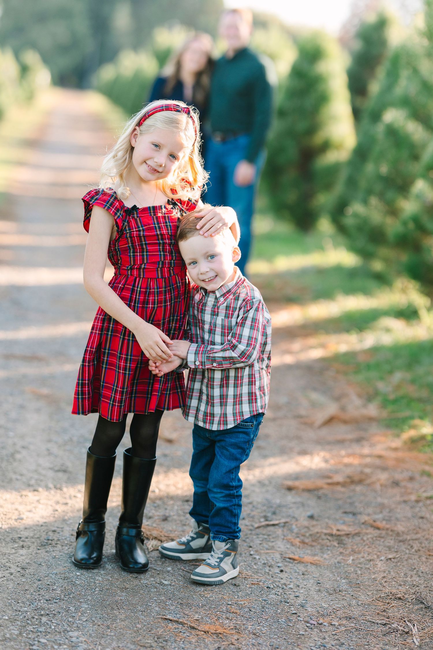 Two children in plaid outfits pose at a Christmas tree farm mini with parents standing in the background with Jessica Heuer photography