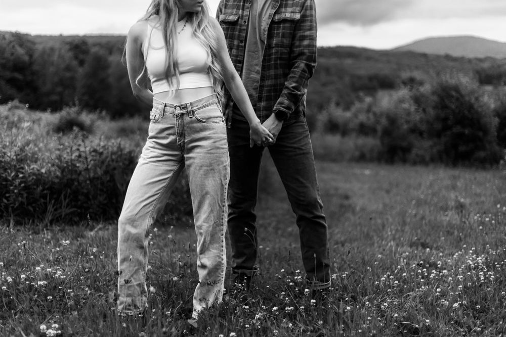 Black and white photo of a couple holding hands in a flower field with mountains in the background.