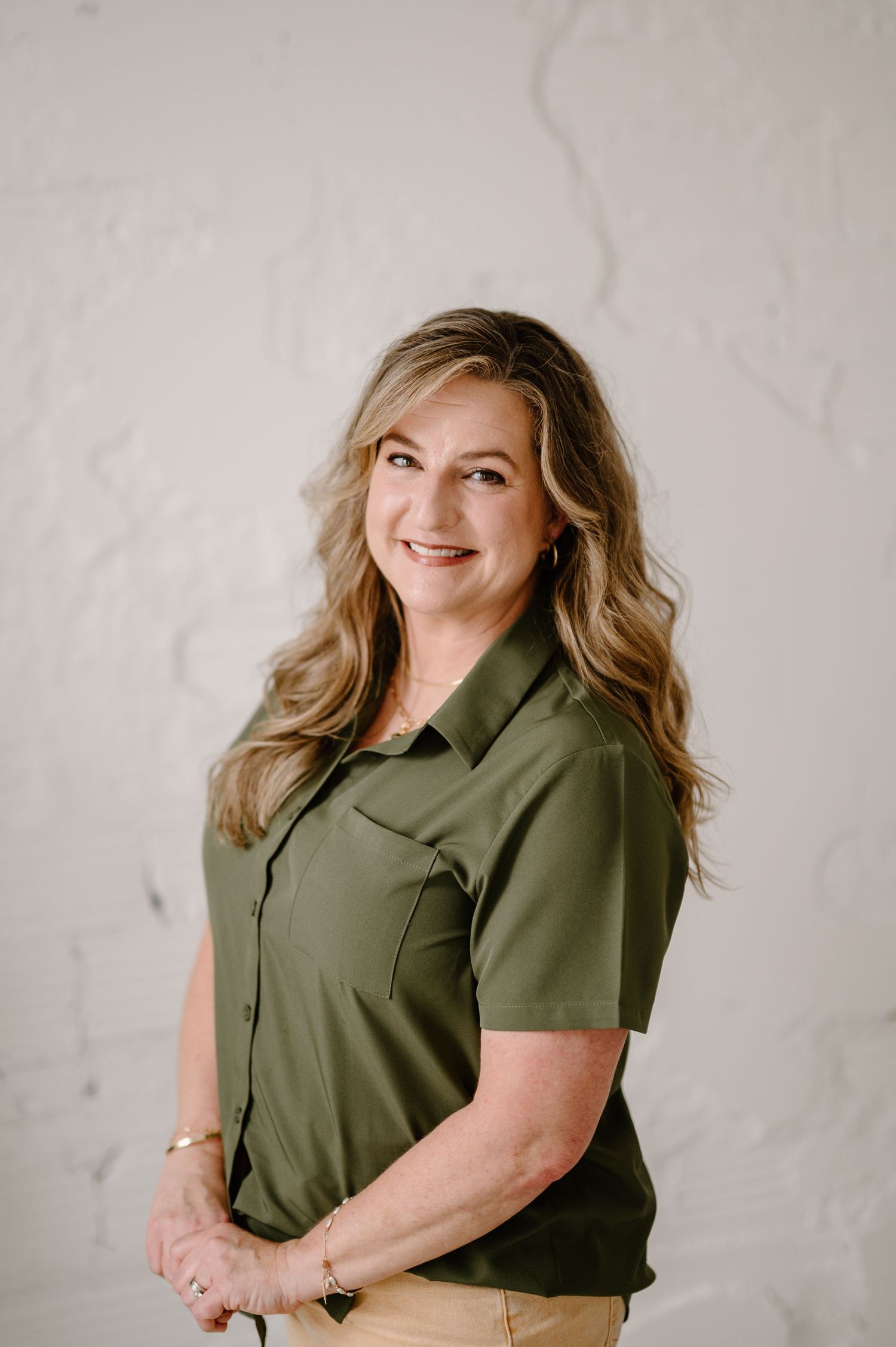 Professional woman in olive green shirt smiling confidently against a white textured background.