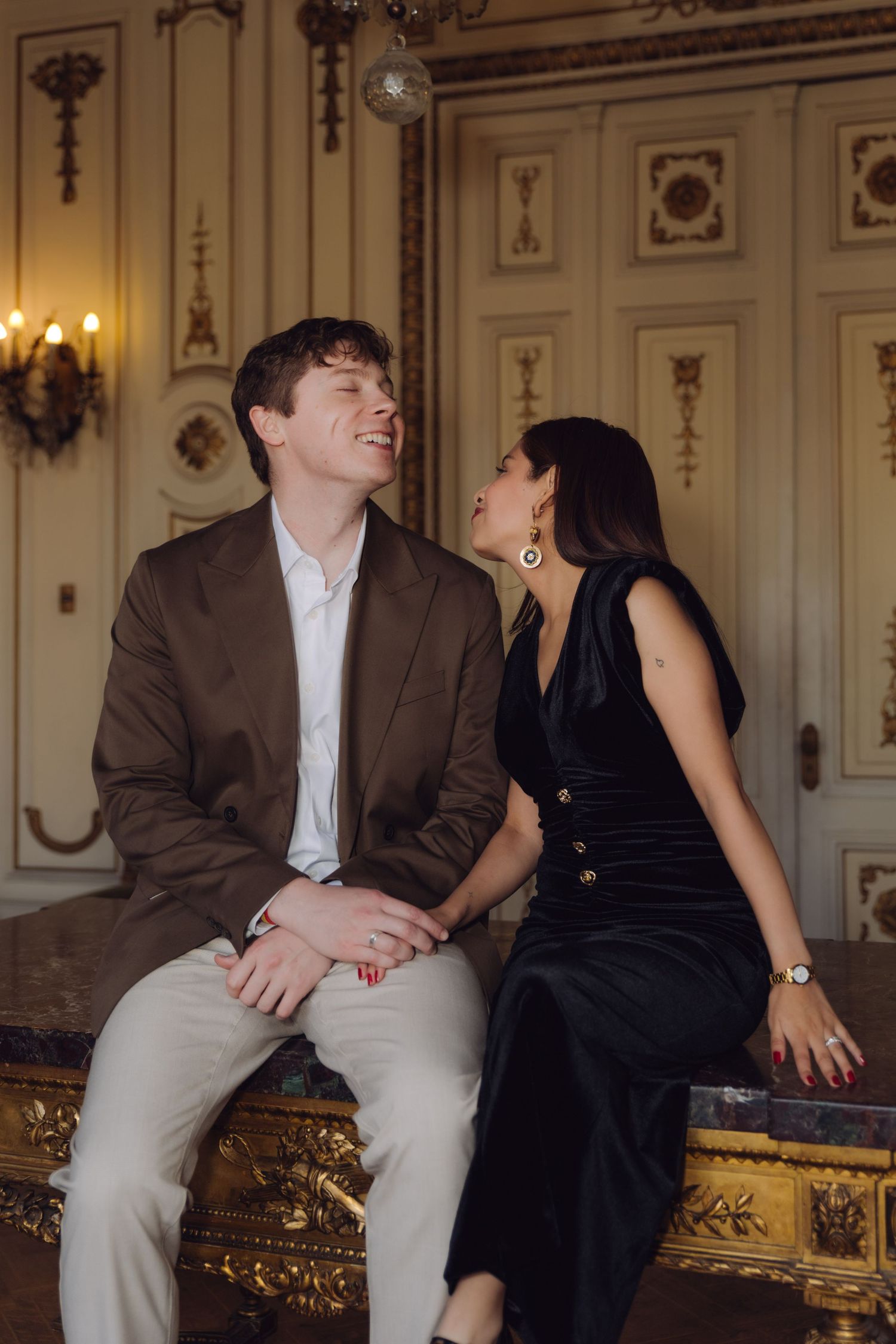 Laughing couple in formal attire sharing a joyful moment in a luxurious baroque-style interior.