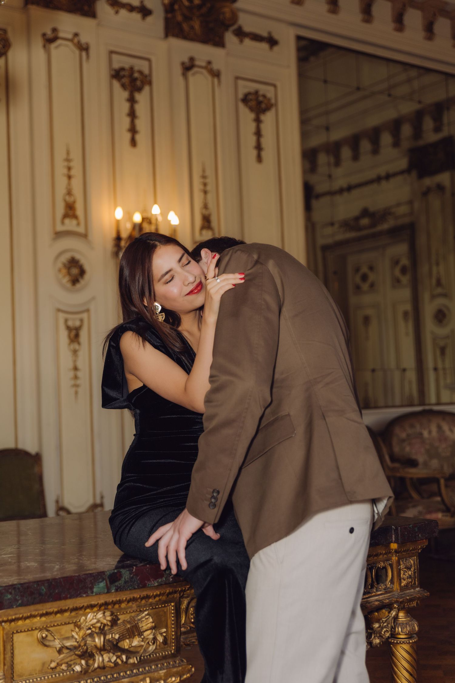 Intimate couple embracing passionately in an elegant chandelier-lit room with classical decor.