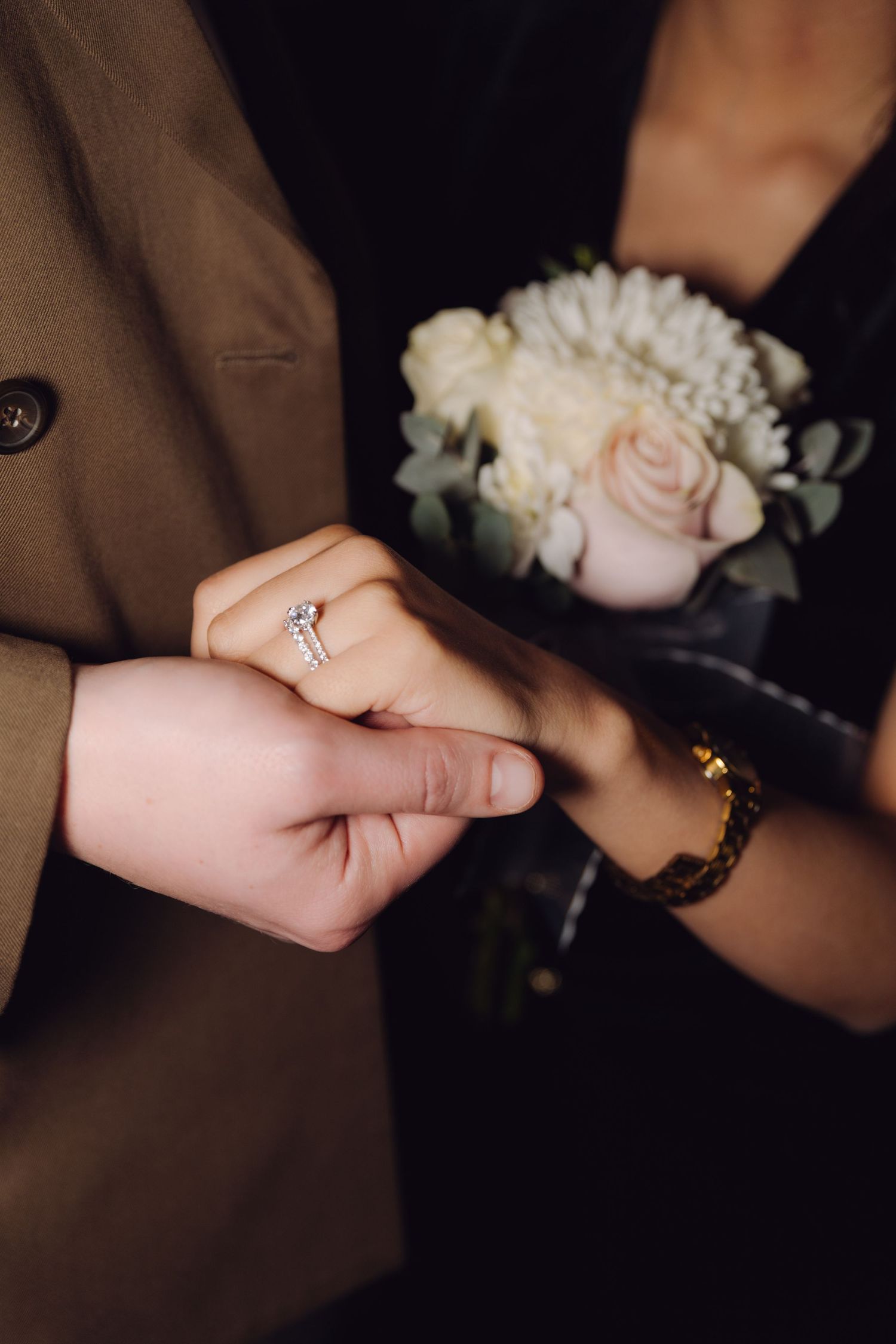 Close-up of diamond engagement ring on bride's hand holding bouquet of white roses and flowers.
