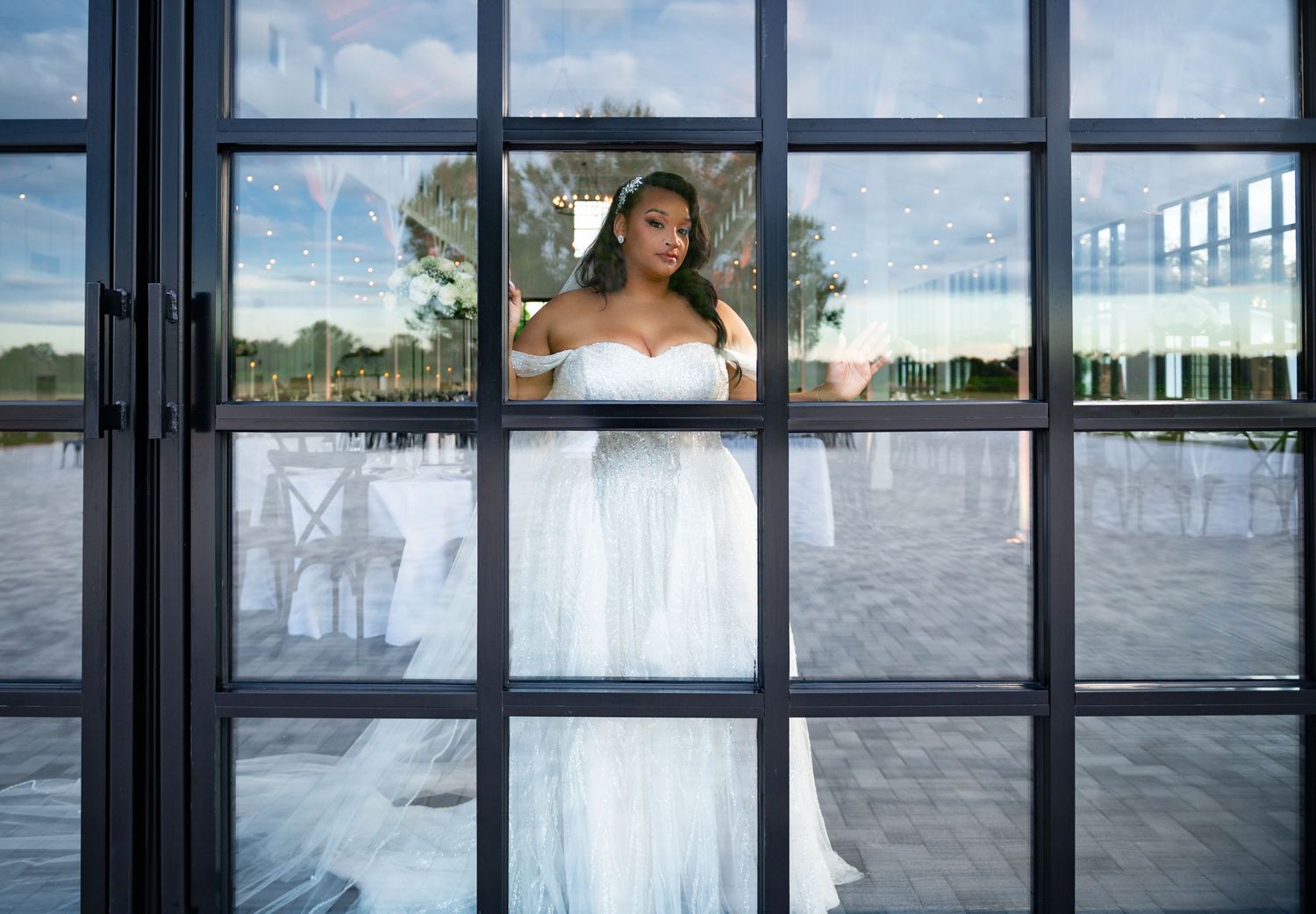 Editorial wedding portrait of the bride standing at a large bay window during her bridal portrait session.