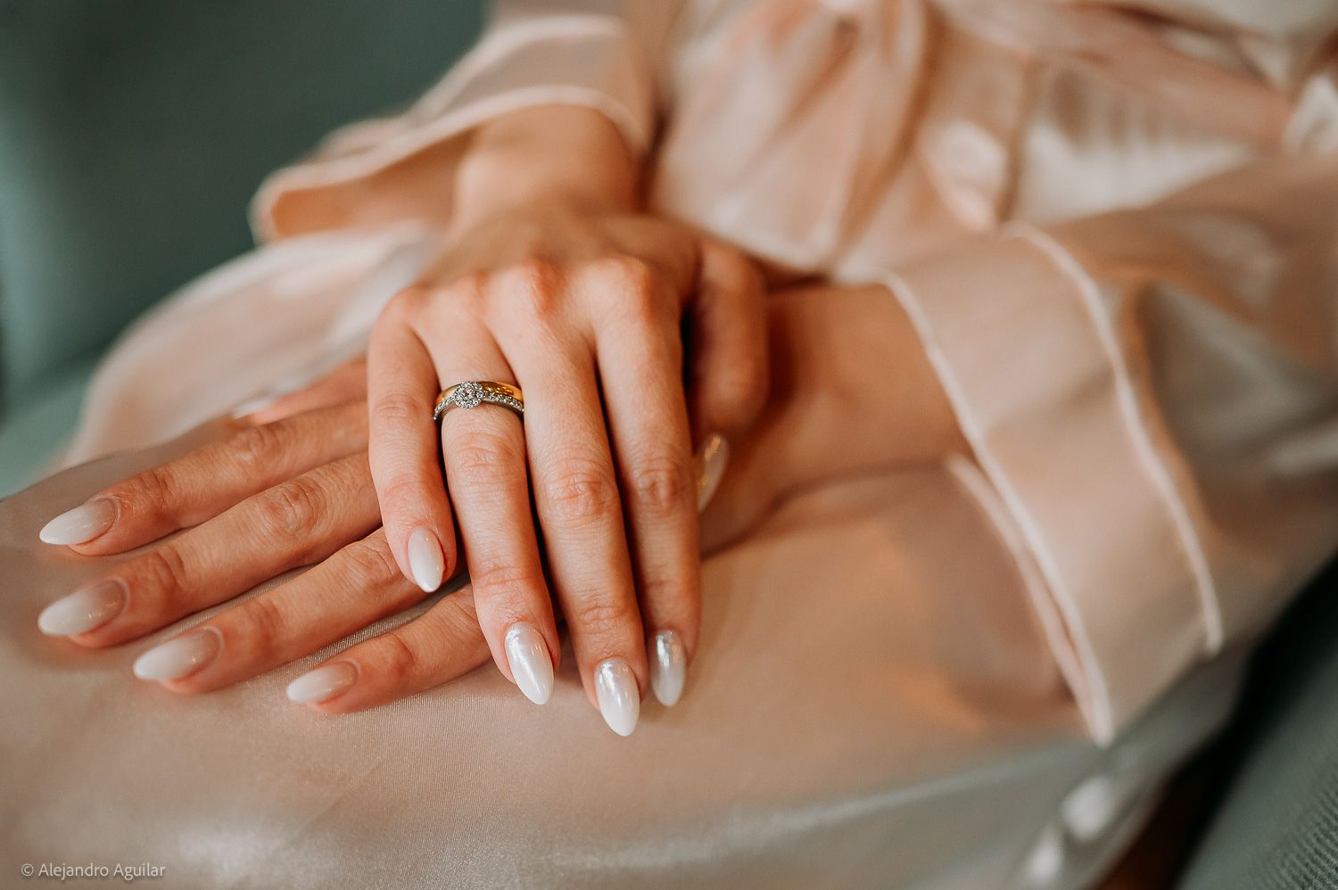 Close-up of bride's hands with white manicure and gold engagement ring on silk robe.
