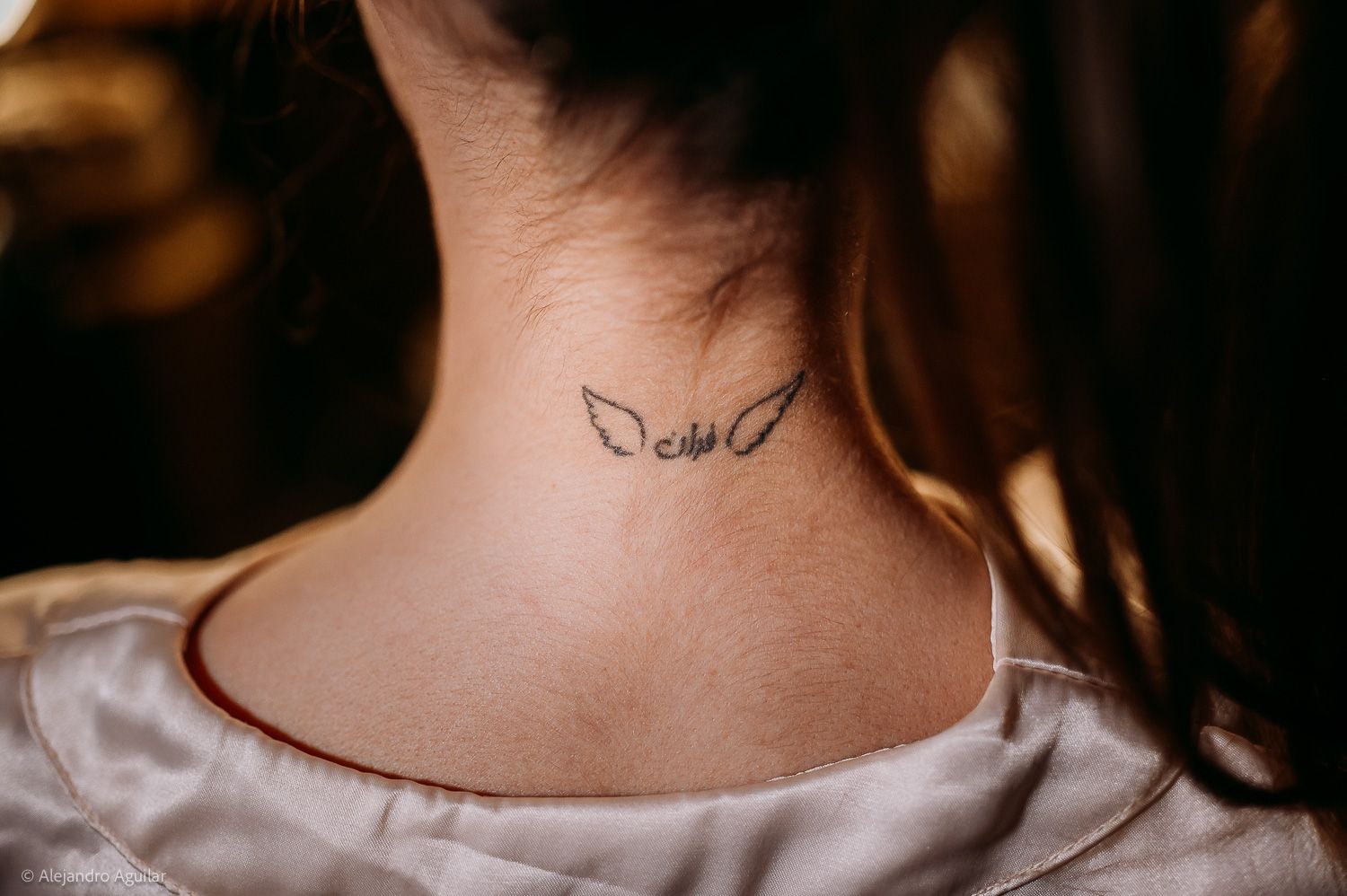 Close-up of a small angel wings tattoo on the back of a woman's neck.
