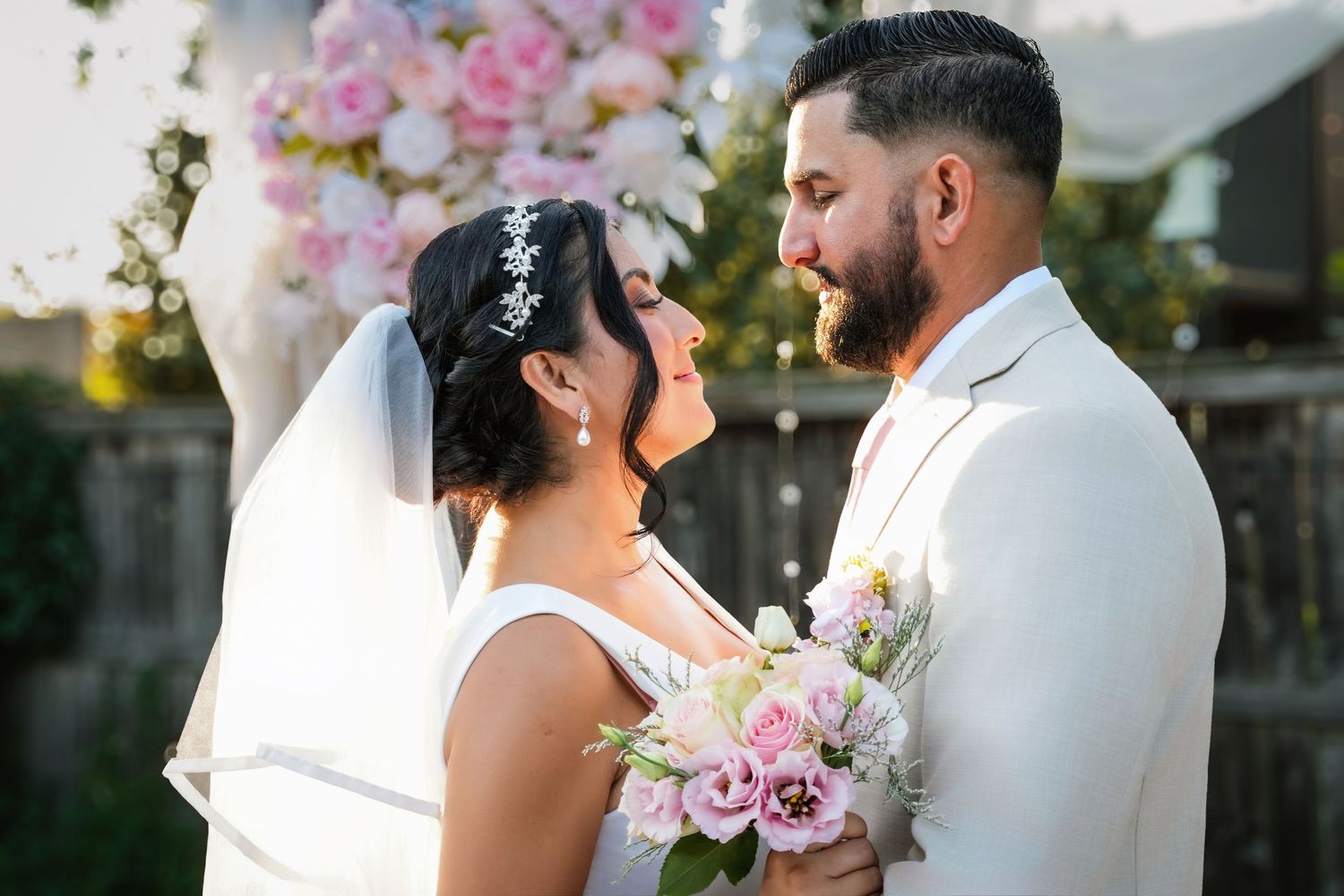 Happy bride and groom smile together outdoors at elegant wedding ceremony with floral arch backdrop.