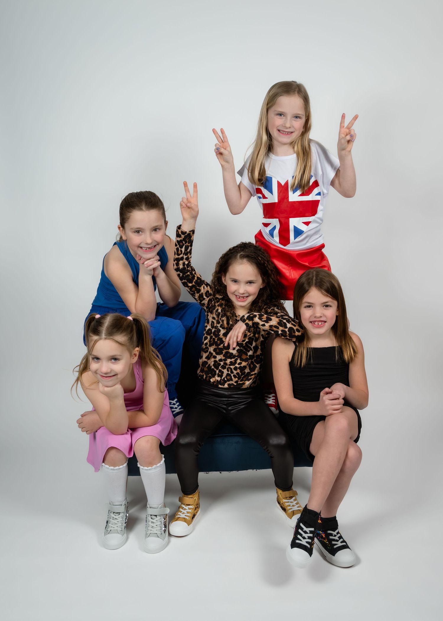 Five young girls pose together in a fun group photo, wearing colorful outfits including a Union Jack shirt.