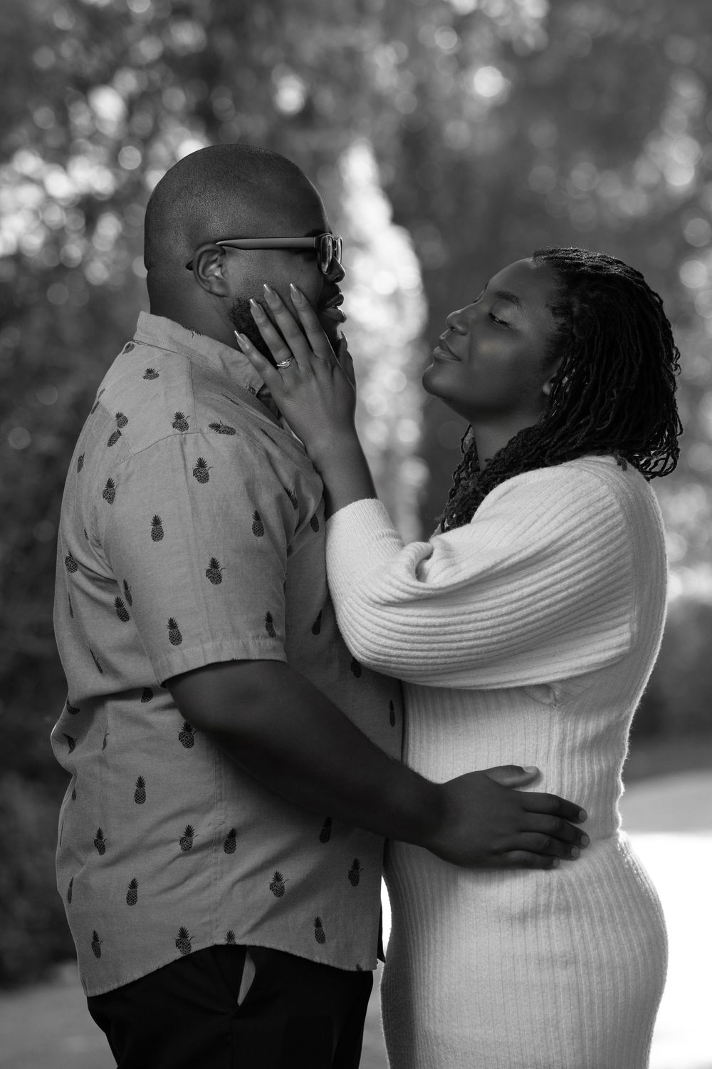 Black and white photo of a couple embracing tenderly outdoors, woman gently touching mans face.