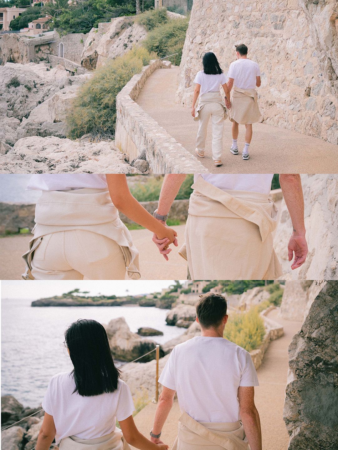 Couple walking hand in hand along a narrow rocky coastal path with ocean views behind them.