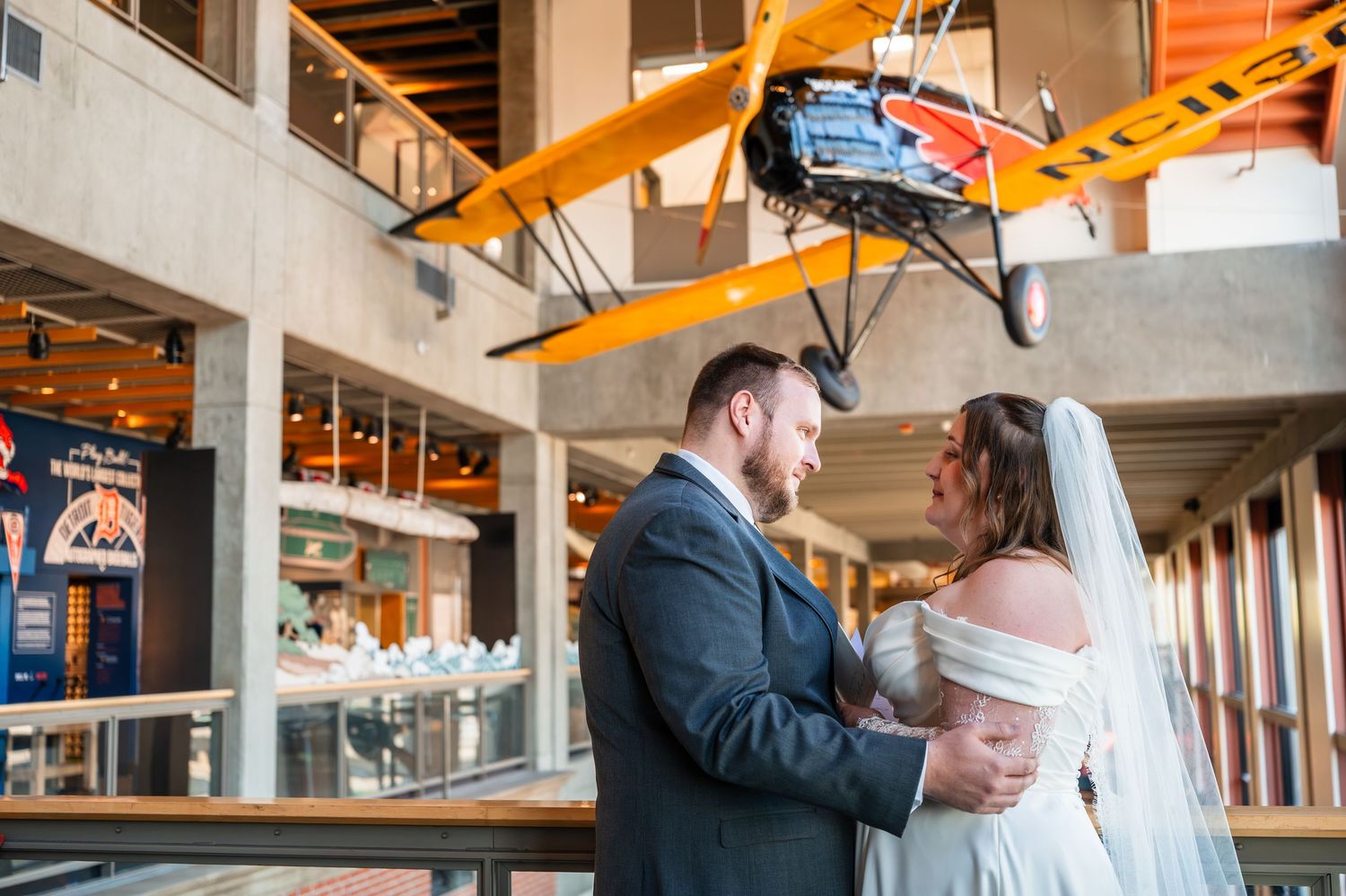 Bride and groom share a romantic moment beneath a vintage yellow biplane at a museum wedding.