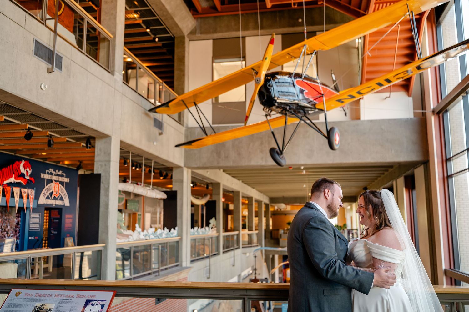Bride and groom share a tender moment beneath a vintage yellow biplane inside a museum wedding venue.