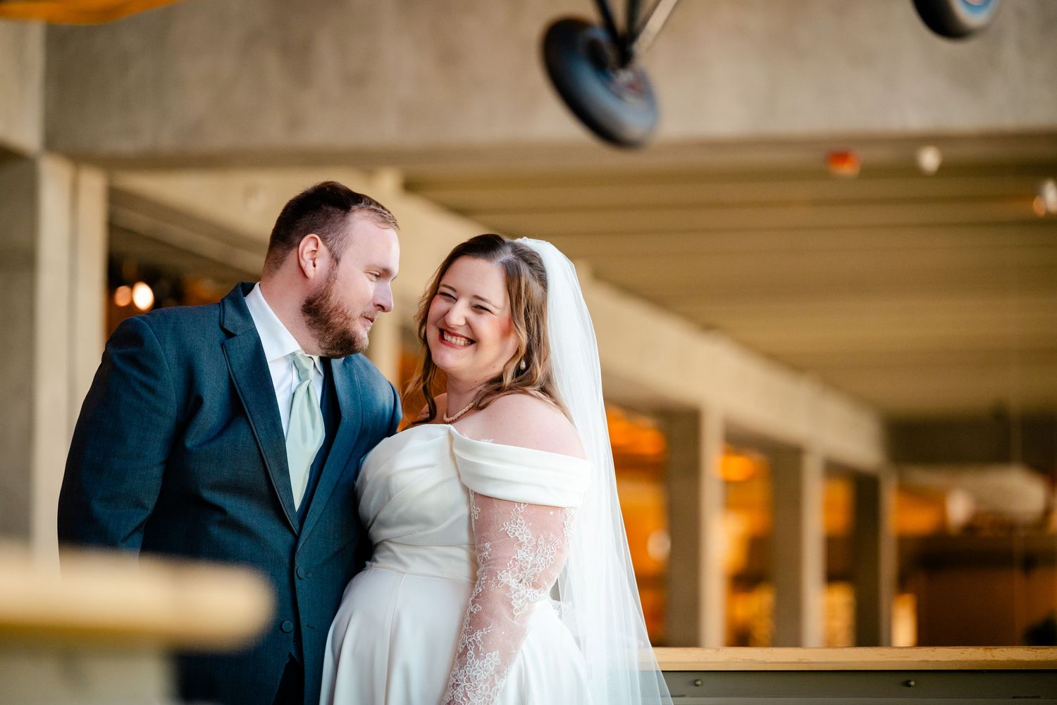 Smiling bride and groom share a tender moment on a balcony at their indoor wedding venue.