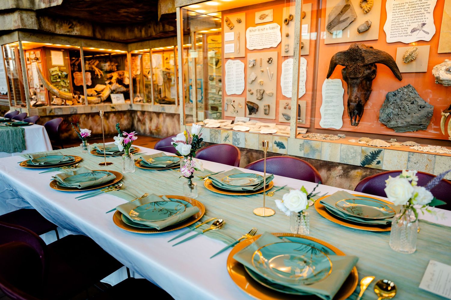 Elegant wedding reception table set with teal plates and gold chargers in a natural history museum.
