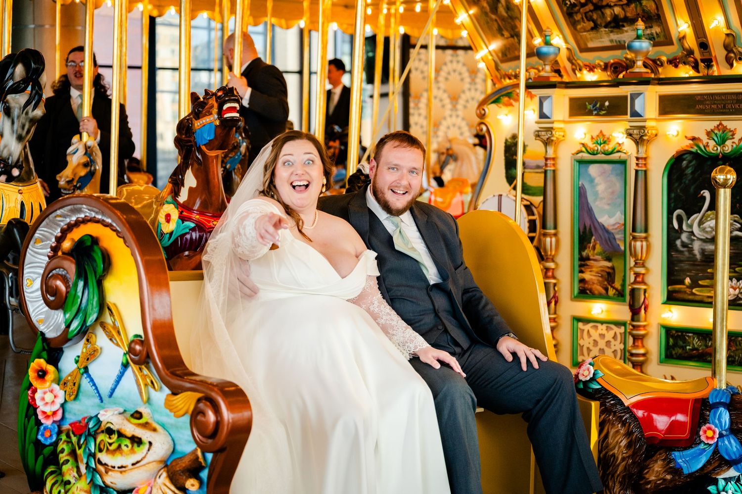 Laughing bride and groom sitting together on a colorful carousel during their wedding celebration.