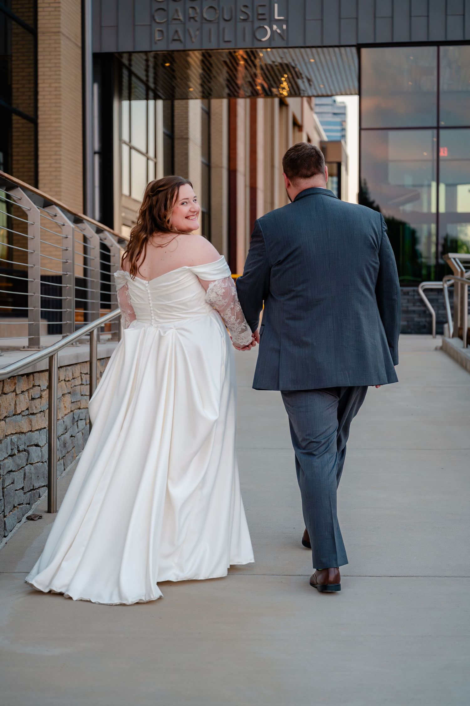 Bride and groom walk hand in hand outside the Carousel Hamilton building after wedding.