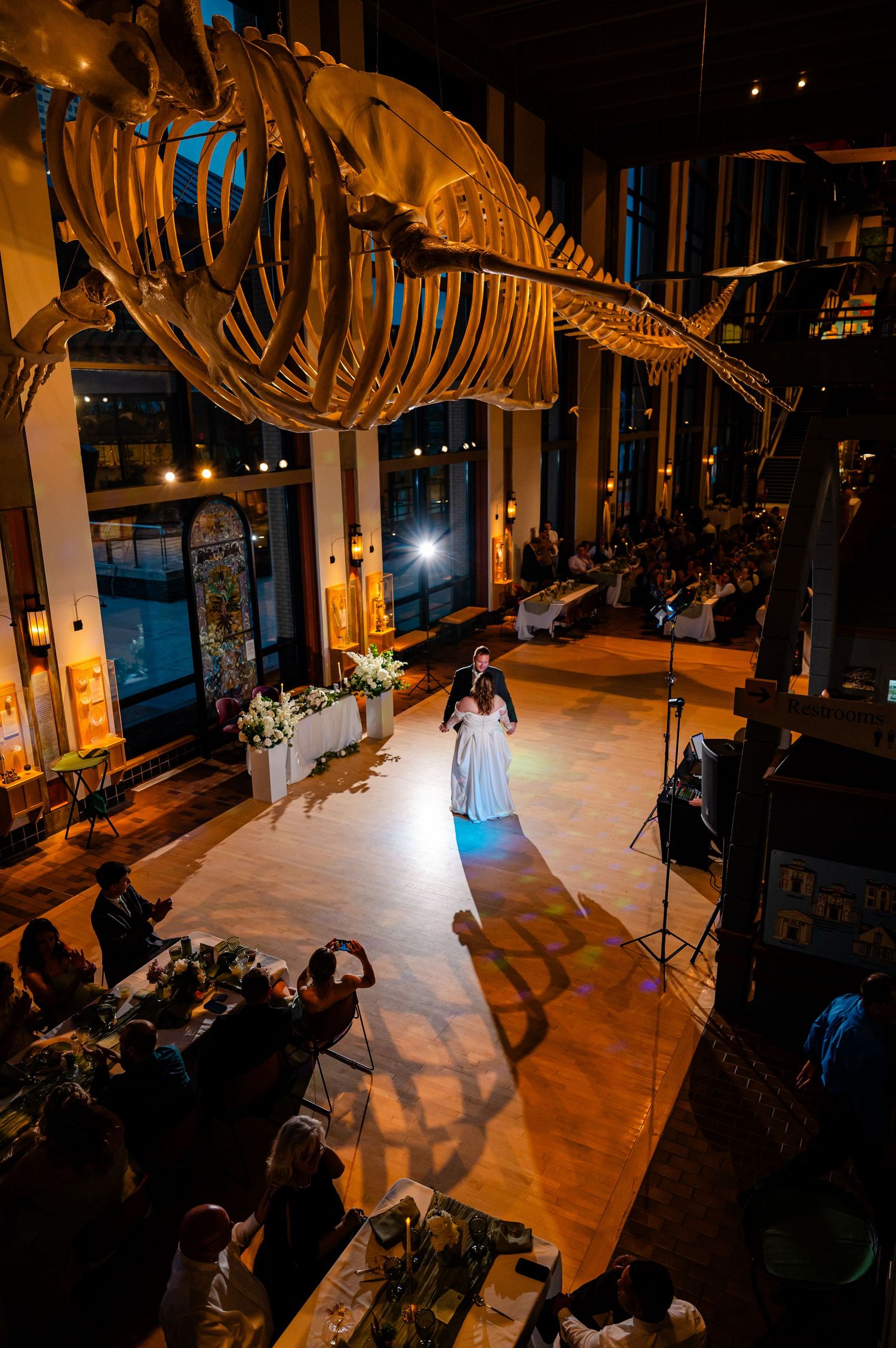 Bride dancing solo under a dramatic whale skeleton display at a museum wedding reception.