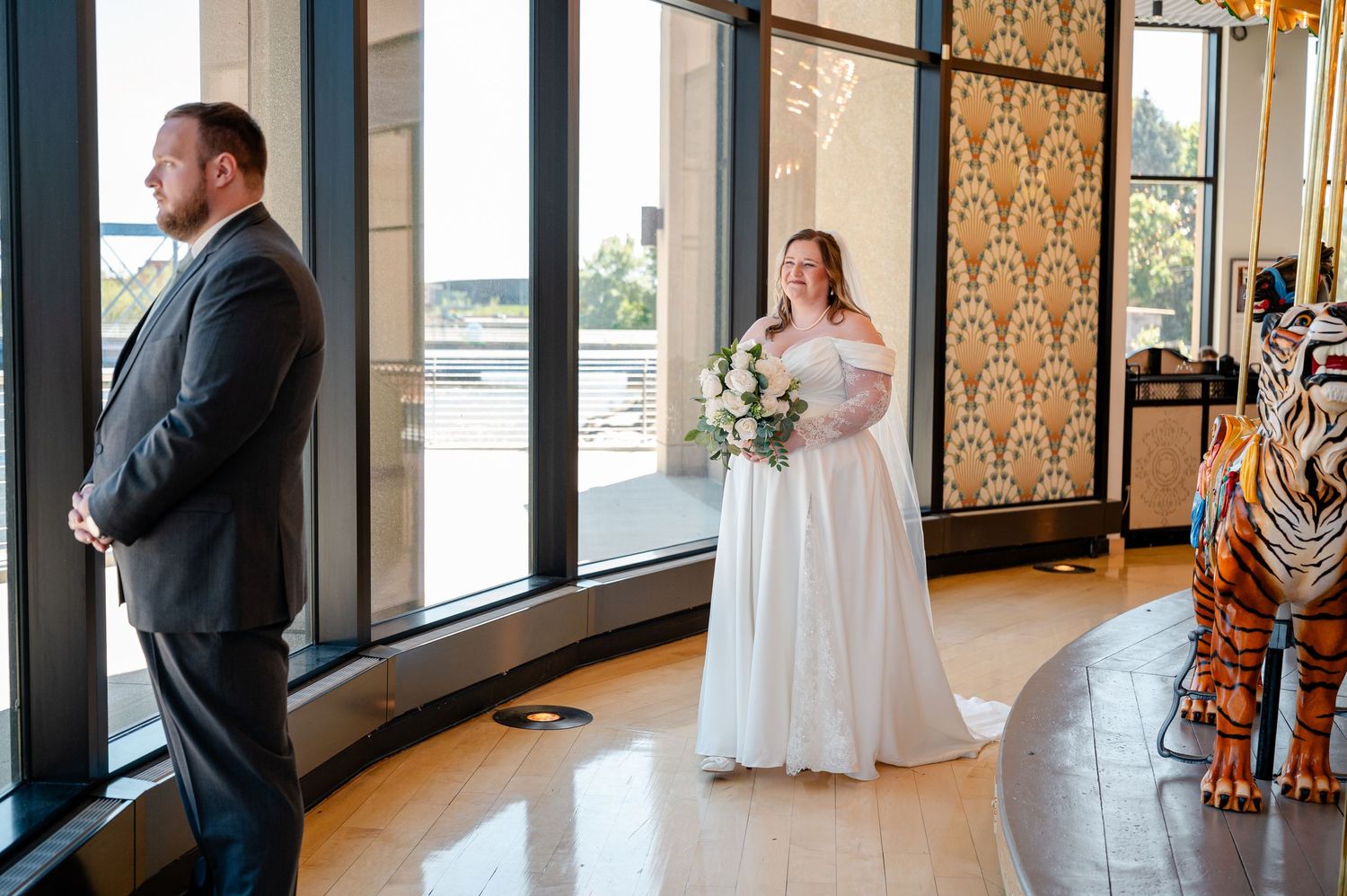 Bride in white off-shoulder gown holds bouquet during first look moment in elegant venue with carousel.