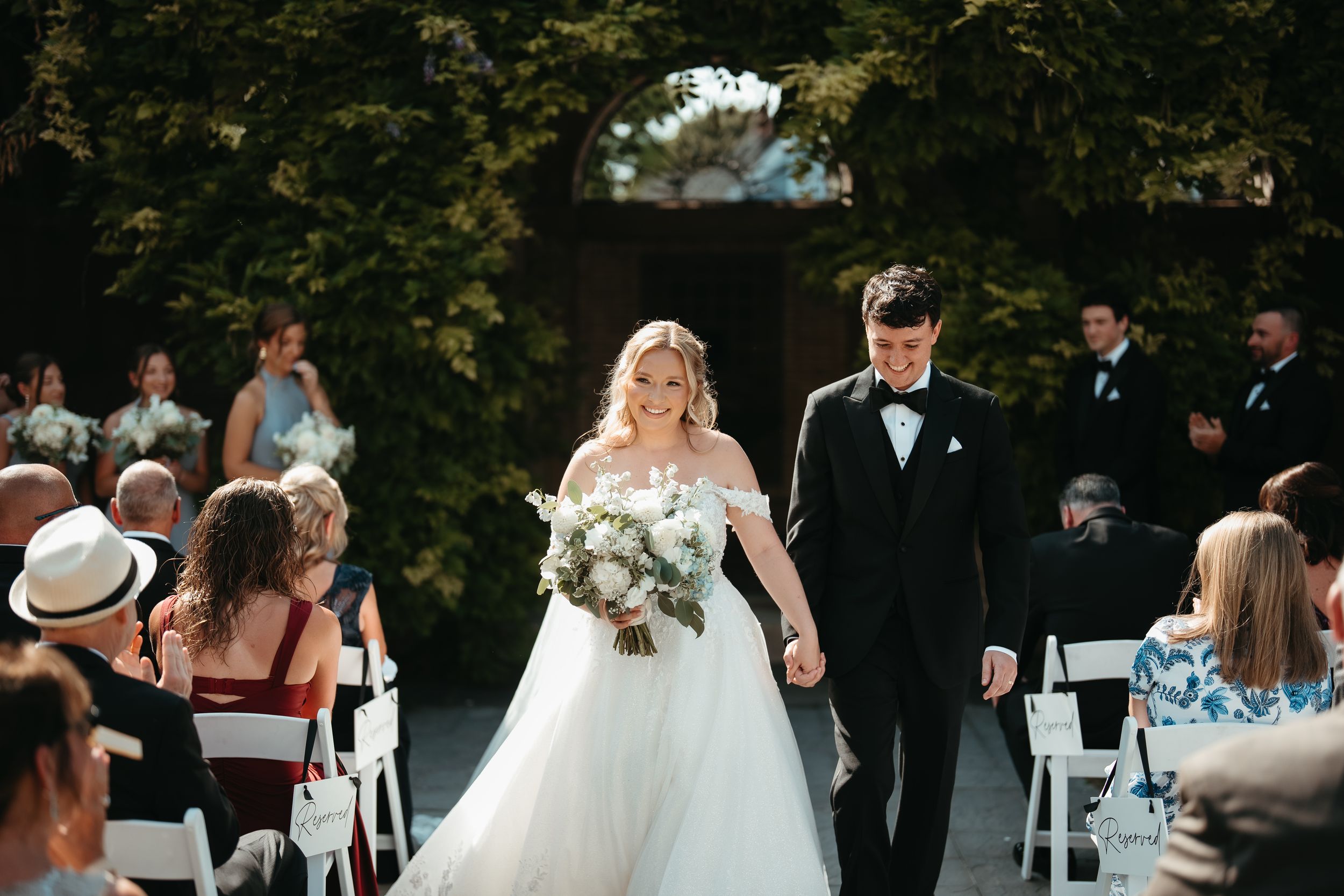 Bride and groom walk down the aisle hand in hand at an elegant outdoor wedding ceremony with guests seated.