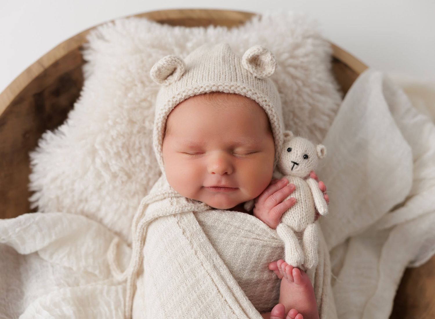 Peaceful newborn baby girl sleeping on white bedding wearing a white outfit and bow headband.
