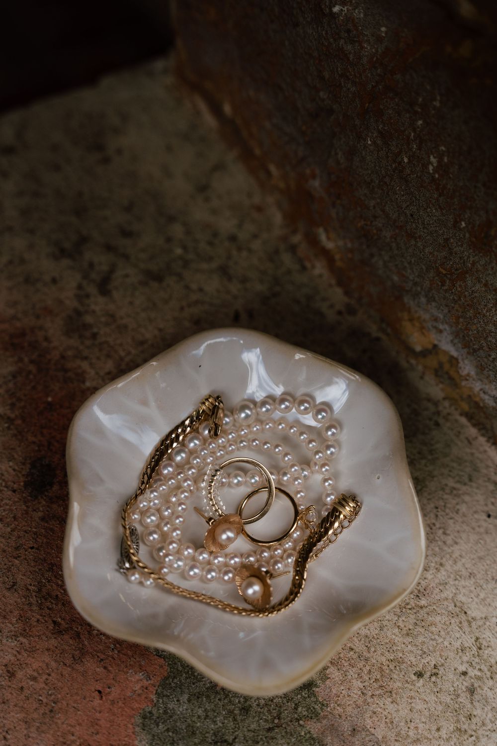Wedding rings nestled in a pearly white shell dish with delicate pearl jewelry on rustic surface.