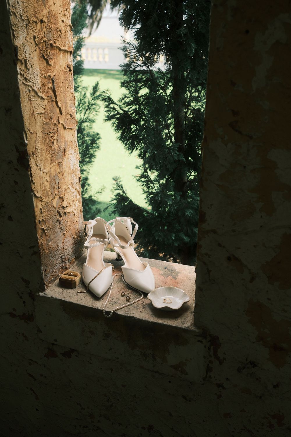 White bridal shoes placed on a rustic stone windowsill with natural lighting.