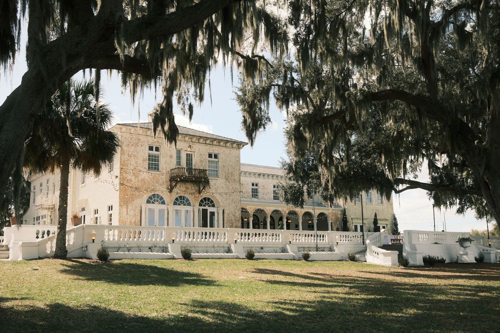 A panoramic view of a historic mansion with Spanish moss draped oak trees in the foreground.
