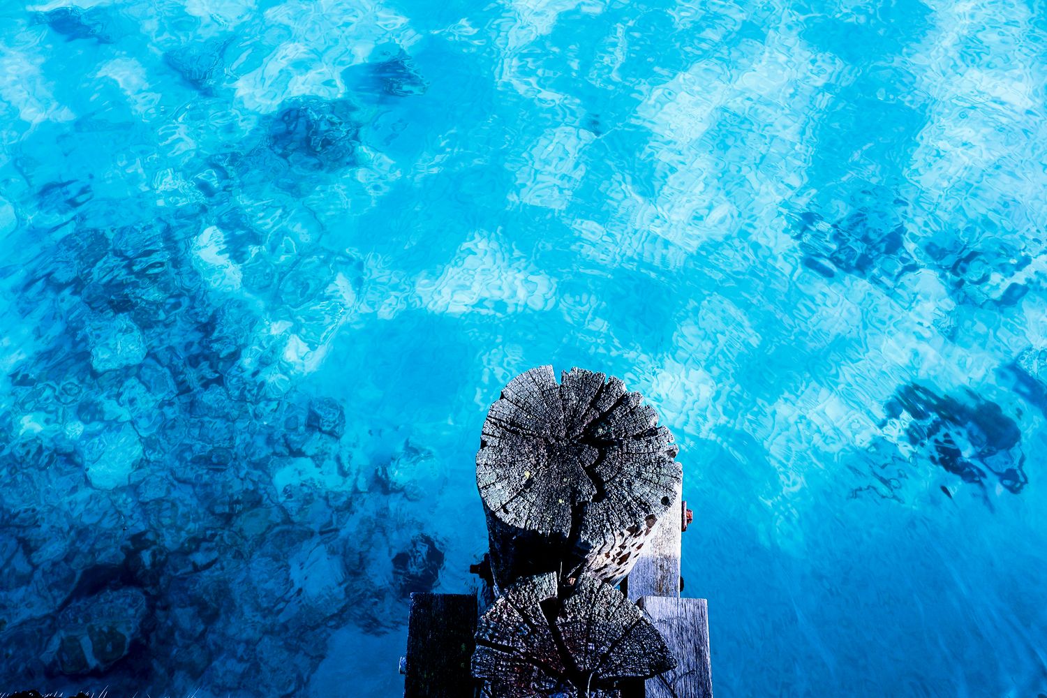 Aerial view of a weathered wooden dock post submerged in vibrant turquoise blue crystal clear water.