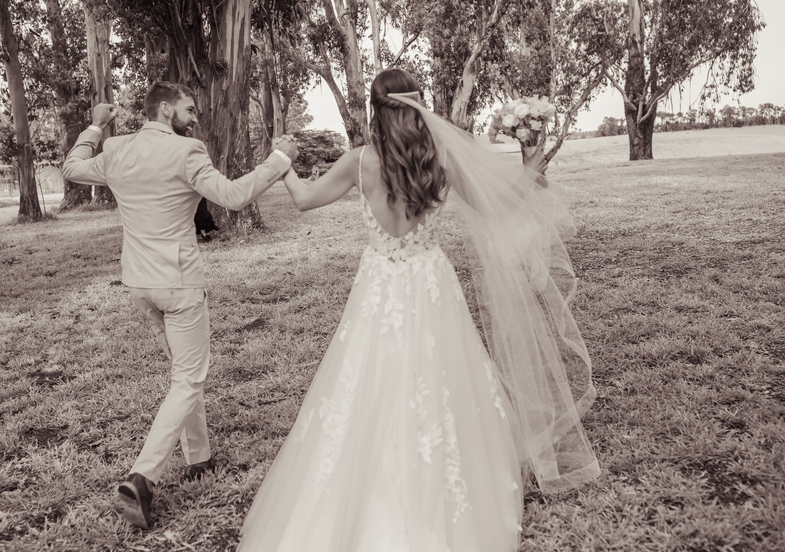 Black and white photo of bride and groom dancing outdoors on their wedding day, with flowing veil and lace gown.