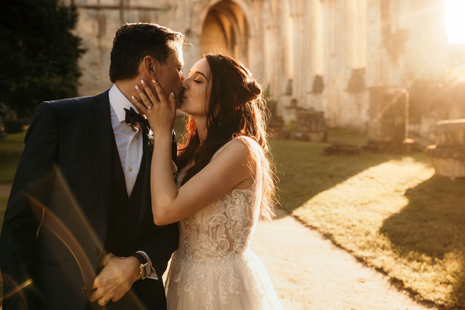Romantic sunset wedding portrait by stone ruins with golden sunlight filtering through.