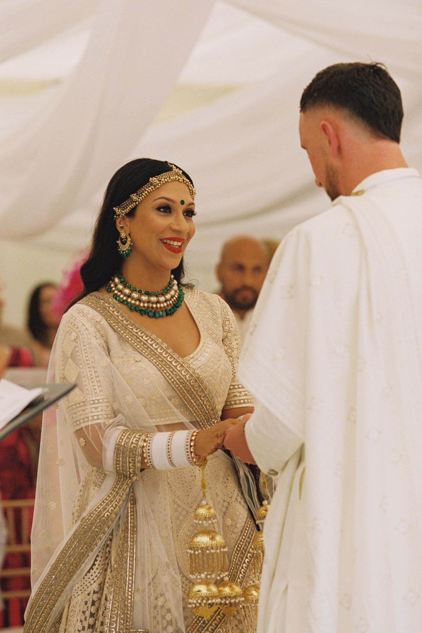 Beautiful bride in ornate Indian bridal attire smiles during traditional wedding ceremony.