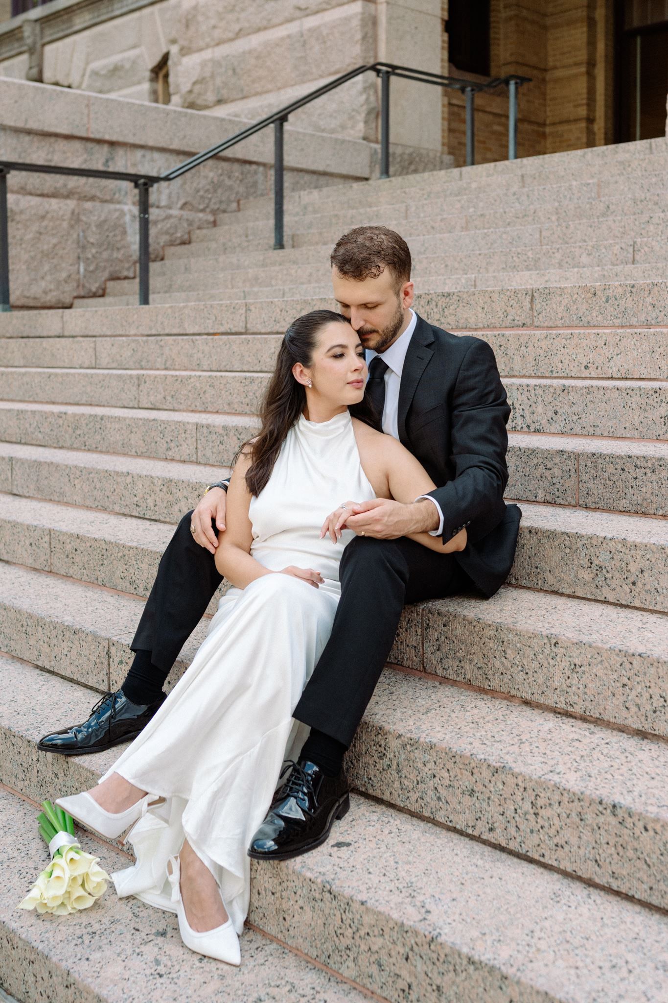 Bride and groom closely sitting together on the granite steps of the 1910 Harris County Courthouse.