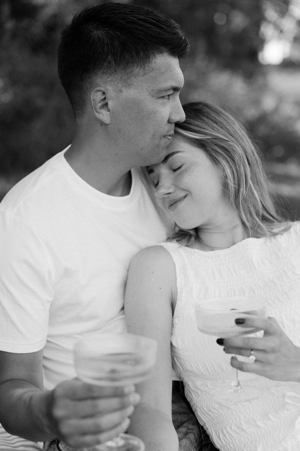 Black and white photo of couple holding drinks and embracing tenderly outdoors.