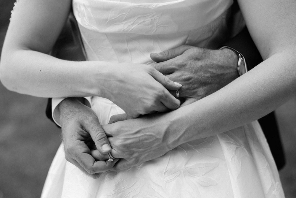 Black and white photo of a couple holding hands, showing wedding rings, bride in white dress.