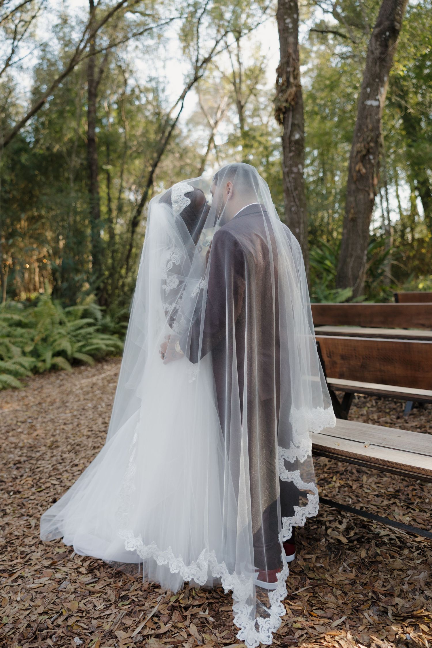 Black and white photo of bride and groom under veil, bride holding floral bouquet with pearls.