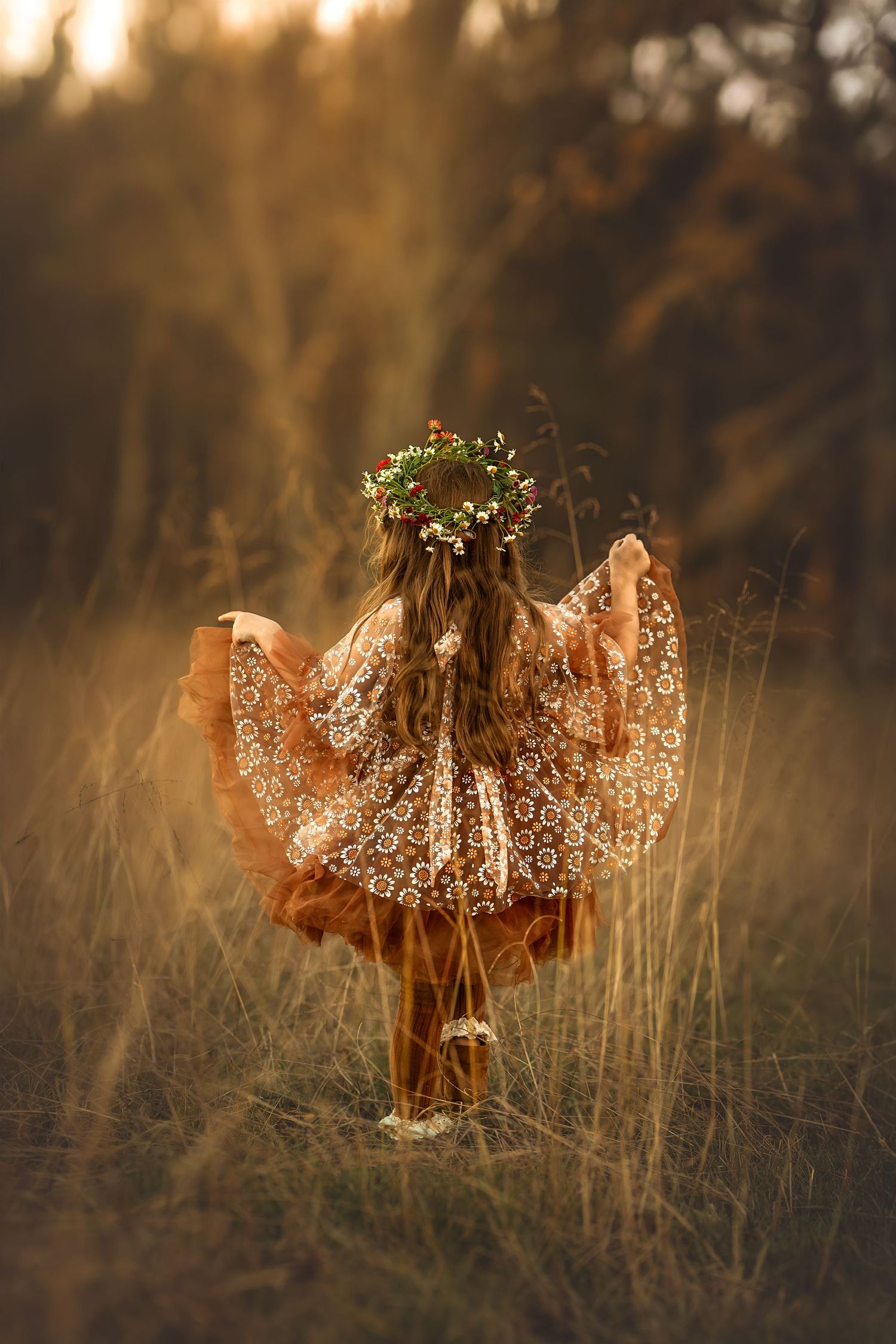 Girl in floral crown and lace dress twirling in golden field at sunset, viewed from behind.