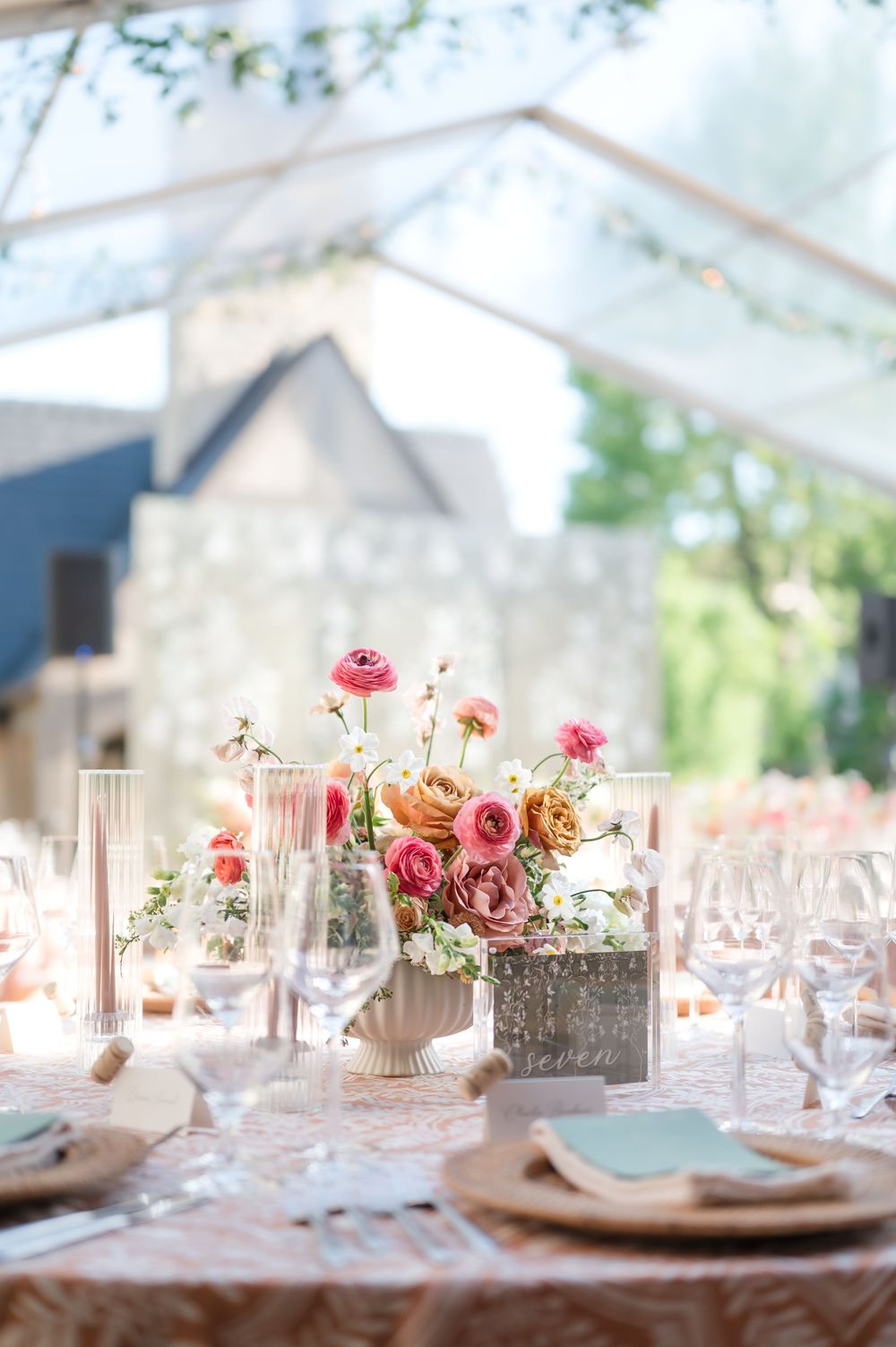 Elegant table setting with pink and peach floral centerpiece in clear vases on lace tablecloth at outdoor wedding reception.