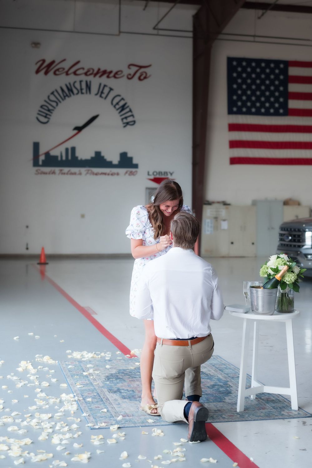 A proposal moment at the Christiansen Jet Center with an American flag in the background.