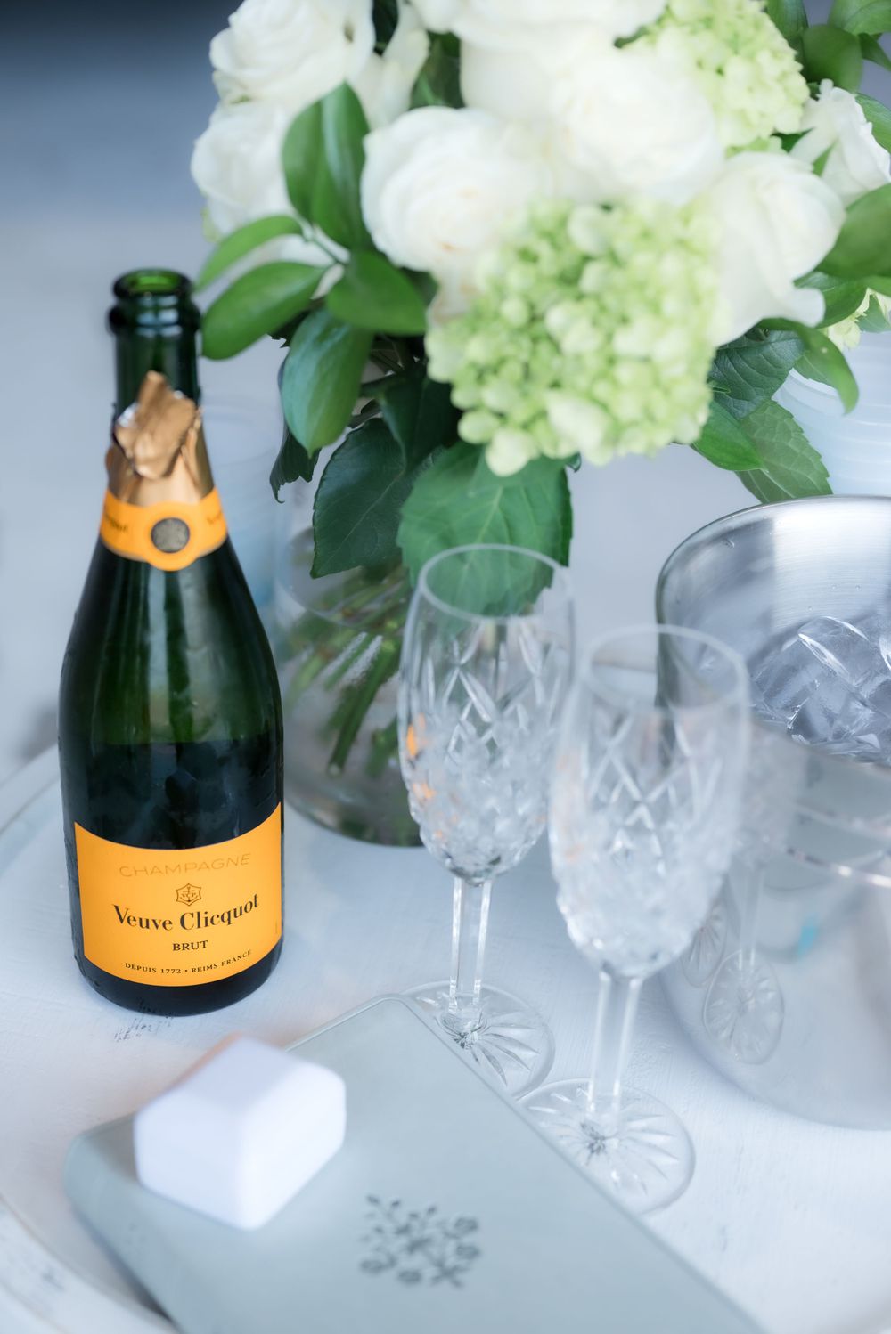 Veuve Clicquot champagne bottle with crystal glasses and white hydrangea flower arrangement.